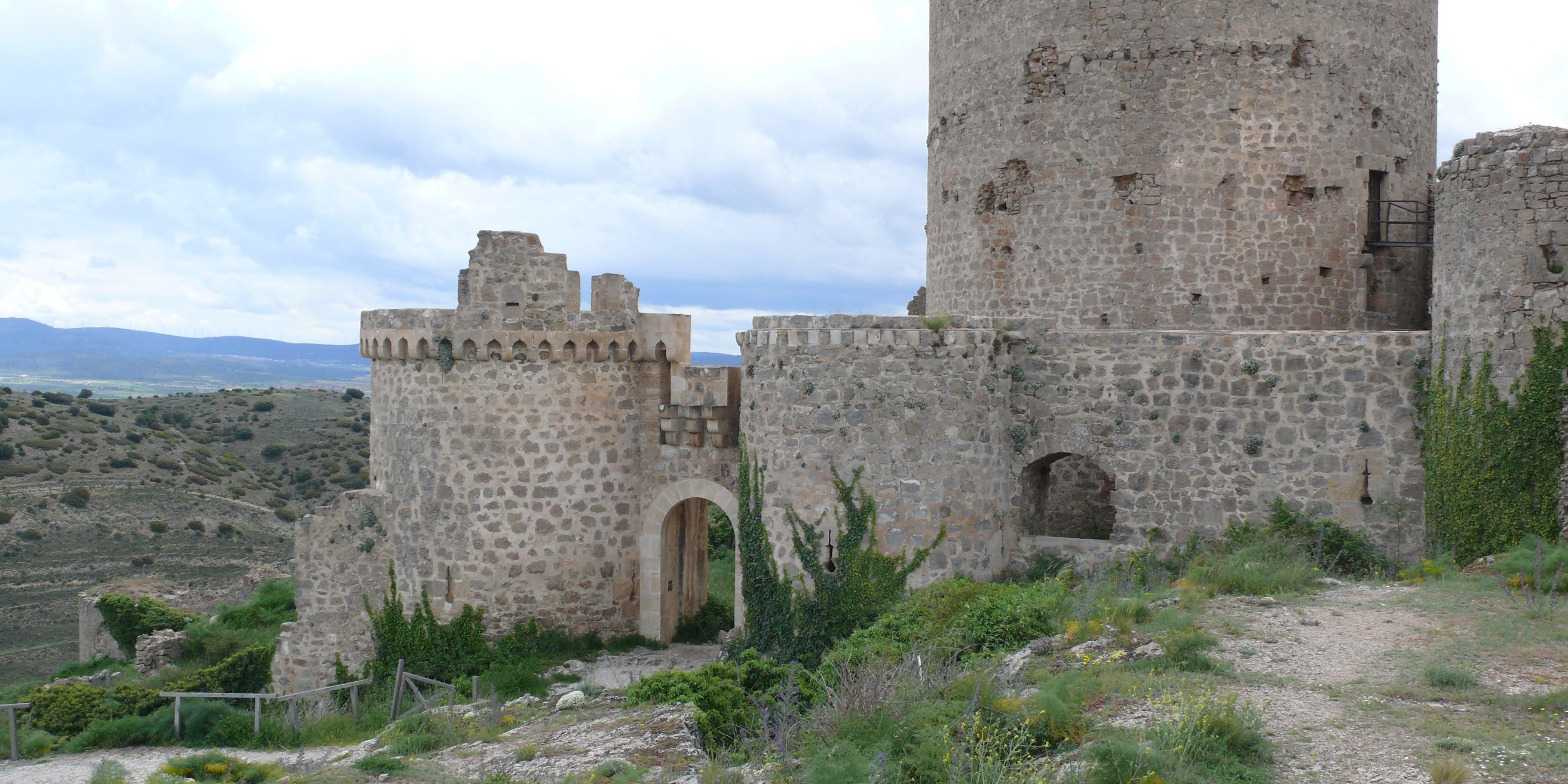 Eine historische Steinschlossburg mit einem hohen Turm und einem Rundbogenportal, eingebettet in eine hügelige Landschaft.