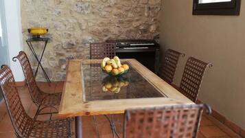 Un coin repas agrémenté d’un mur en pierre, d’une table à plateau en verre, de chaises en osier et d’une petite table sur laquelle est posé un bol.