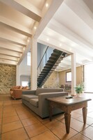 Amplia sala de estar con pared de piedra, una escalera, un sofá, una mesa de centro y una planta en maceta.