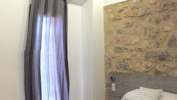 Une chambre à coucher avec un lit, un mur en pierre, une fenêtre avec des rideaux et un sol carrelé.