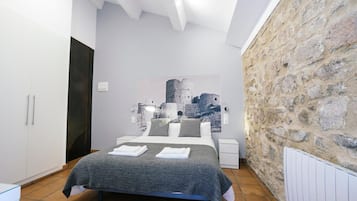 A bedroom with a bed, white wardrobe, stone wall, and a painting of a castle.