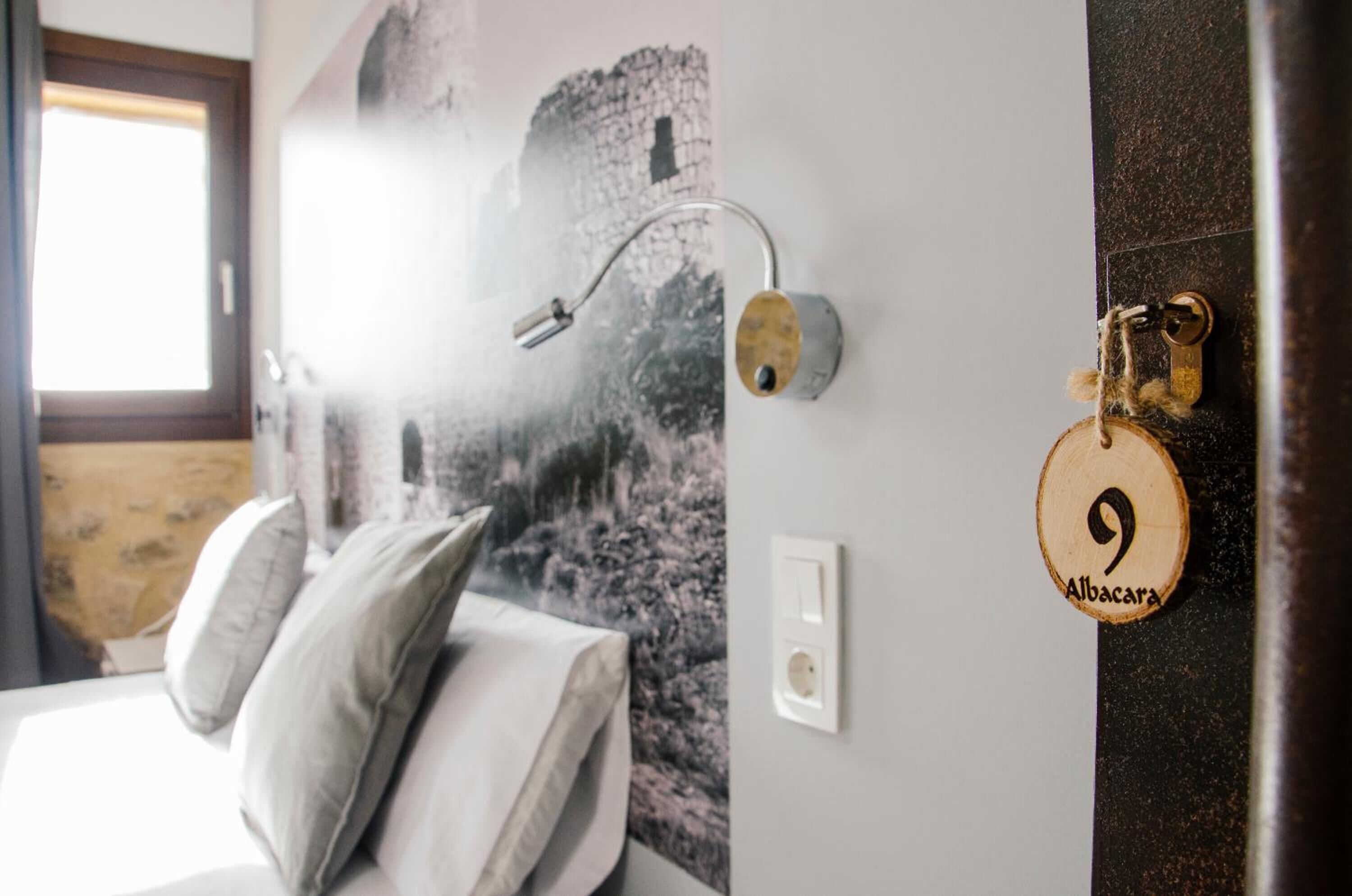 Quarto com cama, travesseiros, luminária na parede e porta com fechadura.