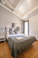 Un dormitorio con una cama grande, una mesita de noche, una lámpara de pared y una obra de arte con temática de castillo.