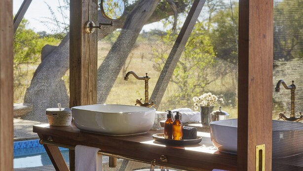 A bathroom with a large white sink, a mirror, and a window overlooking a natural landscape.