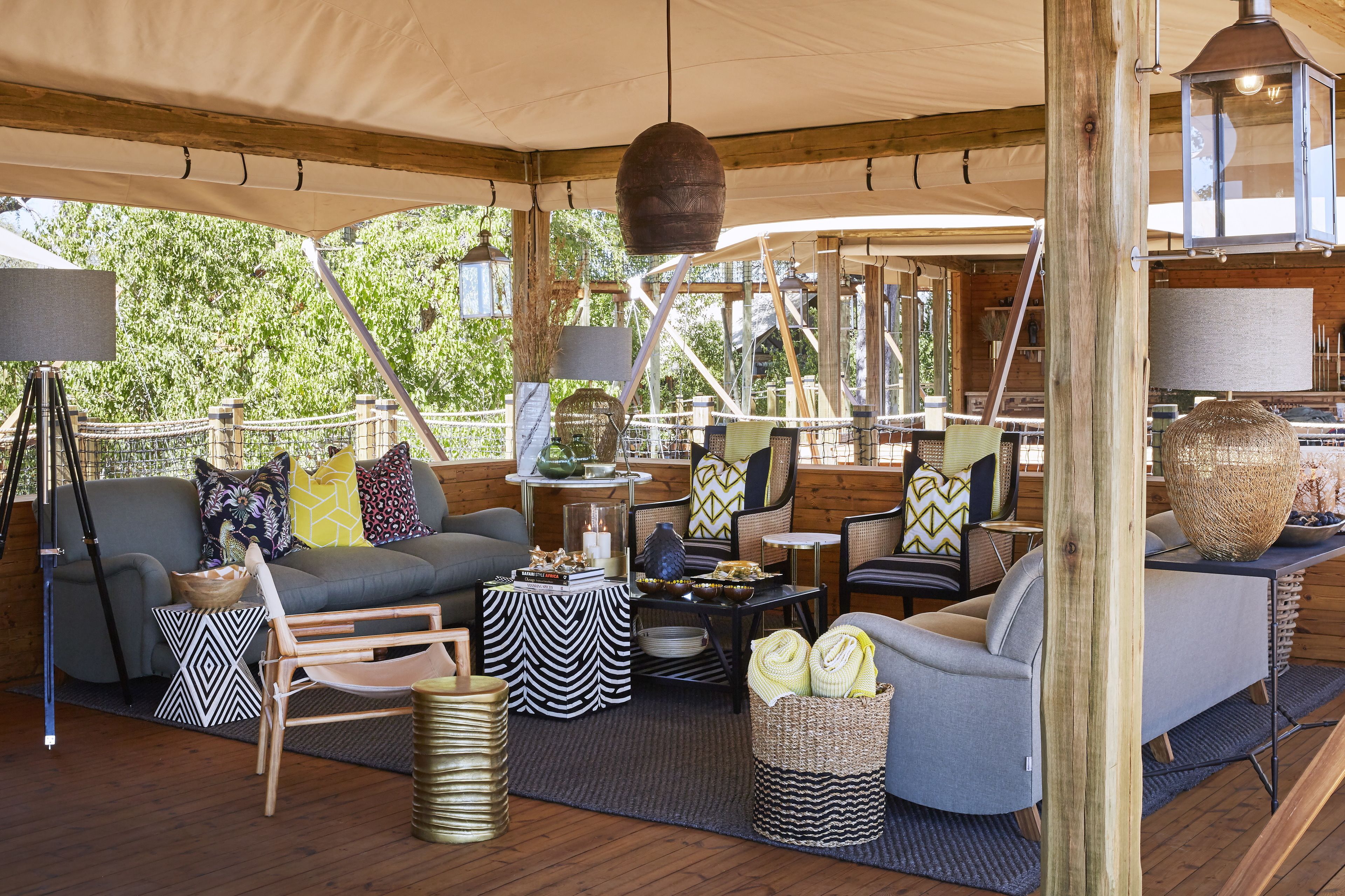 A cozy, well-lit outdoor seating area with a mix of modern and rustic furniture, including a sofa, chairs, and a coffee table, under a large canopy.