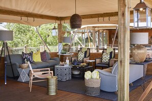 A cozy, well-lit outdoor seating area with a mix of modern and rustic furniture, including a sofa, chairs, and a coffee table, under a large canopy.