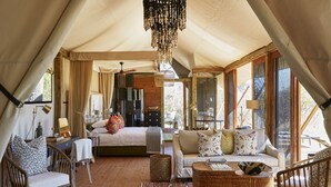 A tented accommodation with a bed, sofa, chairs, and a dining area.