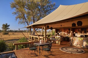 A wooden deck with a table and chairs, a hanging light fixture, and a view of the landscape.