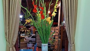 Un tavolo con un servizio da tè e un'composizione floreale in una stanza con mobili in legno e tende.