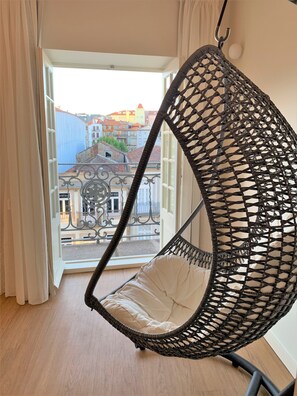 A wicker hanging chair with a cushion, positioned in a room with a view of a building through an open door. - Clérigos Prime Suites by Porto City Hosts (Porto)