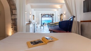 A bedroom with a bed, an open book, a view of the sea, and a boat outside. - Neosikos AmazingBeach House Milos Island (Milos)