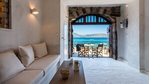 A room with a white sofa, a wooden table, and a view of the sea through an arched doorway. - Neosikos AmazingBeach House Milos Island (Milos)