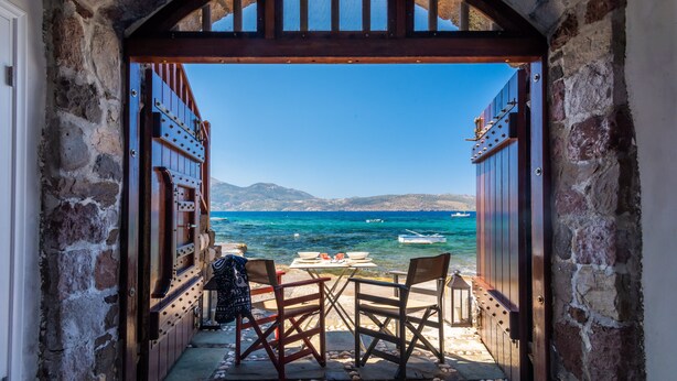 An open doorway leading to a terrace with a table and chairs, overlooking a clear blue sea and distant mountains. - Neosikos AmazingBeach House Milos Island (Milos)