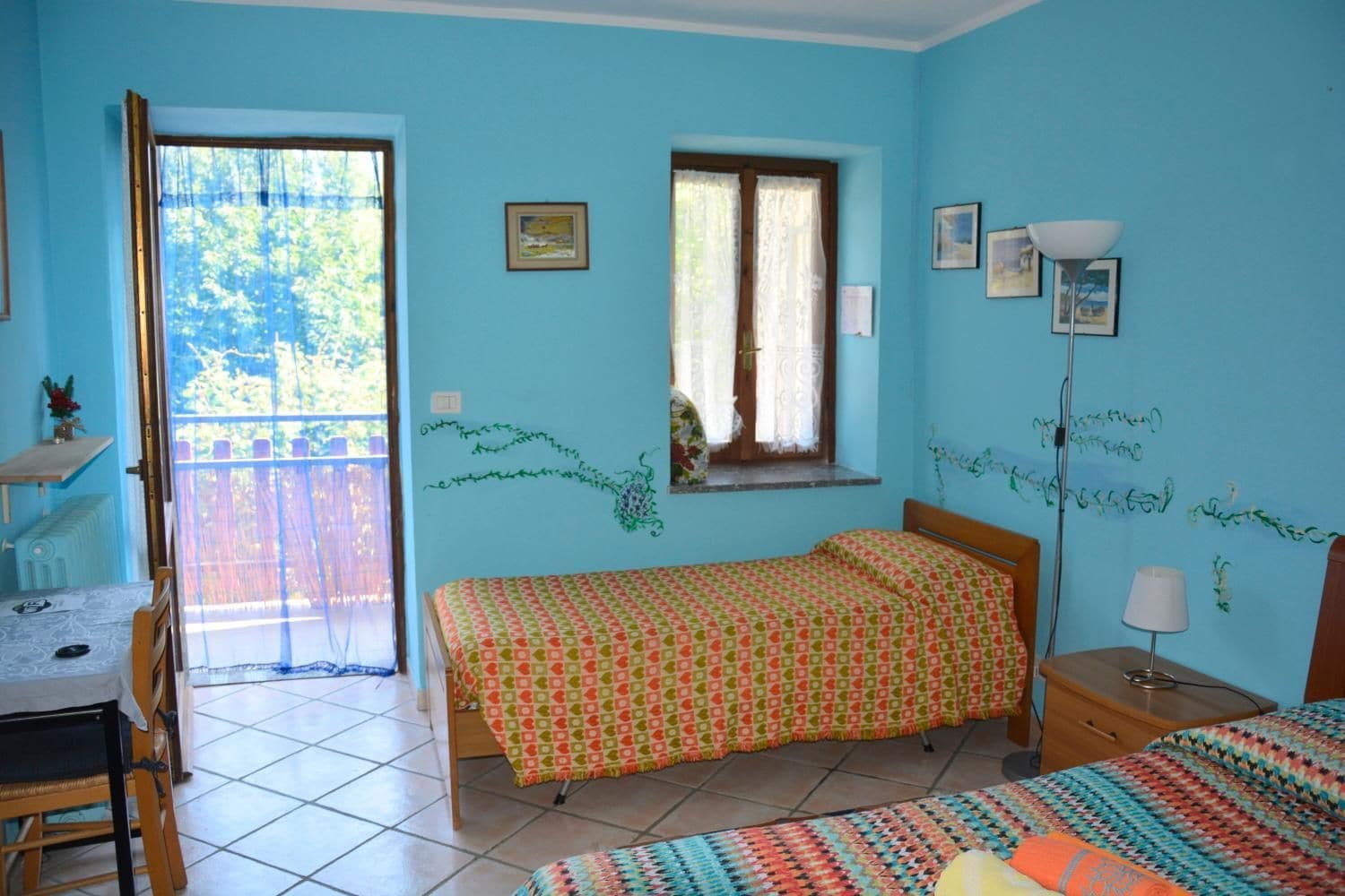 A room with a bed, a desk, a chair, a window with curtains, and a lamp.