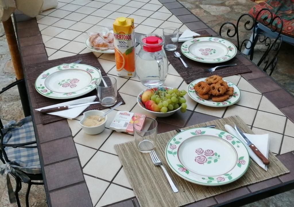 Ein Esstisch ist gedeckt mit Tellern, Besteck, einer Orangensaftflasche, einer Obstschale und einem Glas Wasser.