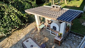A stone patio with a tiled table and chairs, a stone oven, and a pergola with a tiled roof. - Casa Omnia B&B (Castellamonte)