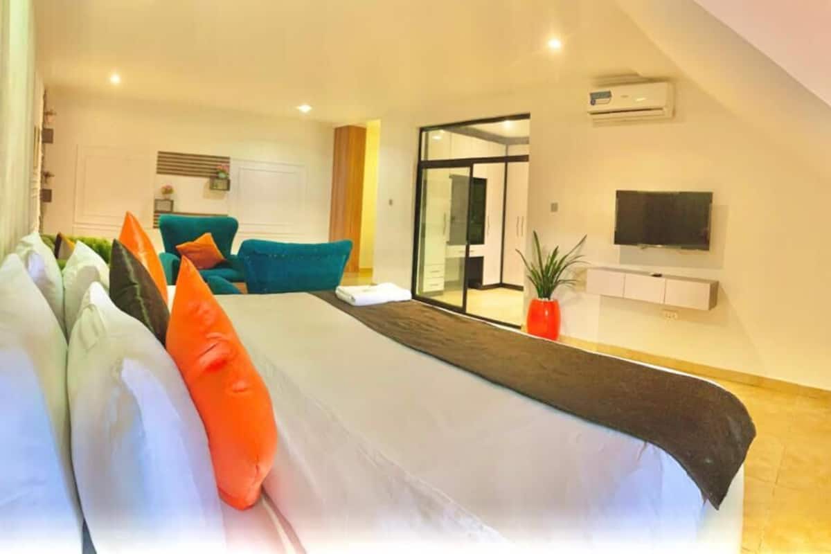 A modern hotel room with a large bed, a TV mounted on the wall, and a sliding glass door leading to a balcony.