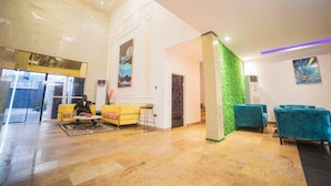 Um hall com piso de mármore, assentos amarelo e azul, uma parede de destaque verde e obras de arte nas paredes.