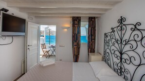 A bedroom with a bed, a TV mounted on the wall, a window with curtains, and a view of the sea. - Beautiful Apartment With Amazing View In Mykonos Old Town (Mykonos)