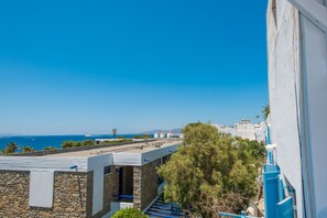 A coastal building with a stone facade, a blue staircase, and a view of the sea and distant buildings.