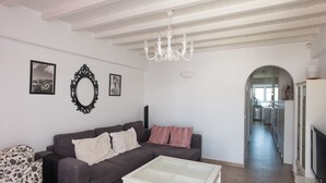 A living room with a sofa, a glass coffee table, a chandelier, and a hallway leading to a kitchen. - Beautiful Apartment With Amazing View In Mykonos Old Town (Mykonos)