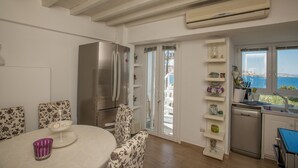 A modern kitchen with a large refrigerator, a dining area with floral chairs, and a view of the sea through the window. - Beautiful Apartment With Amazing View In Mykonos Old Town (Mykonos)