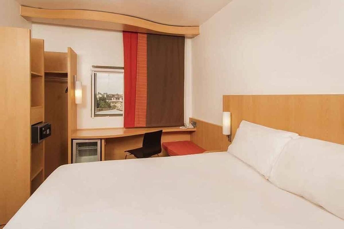 Une chambre d’hôtel équipée d’un lit, d’un bureau, d’une chaise, d’une armoire et d’une fenêtre avec des rideaux.