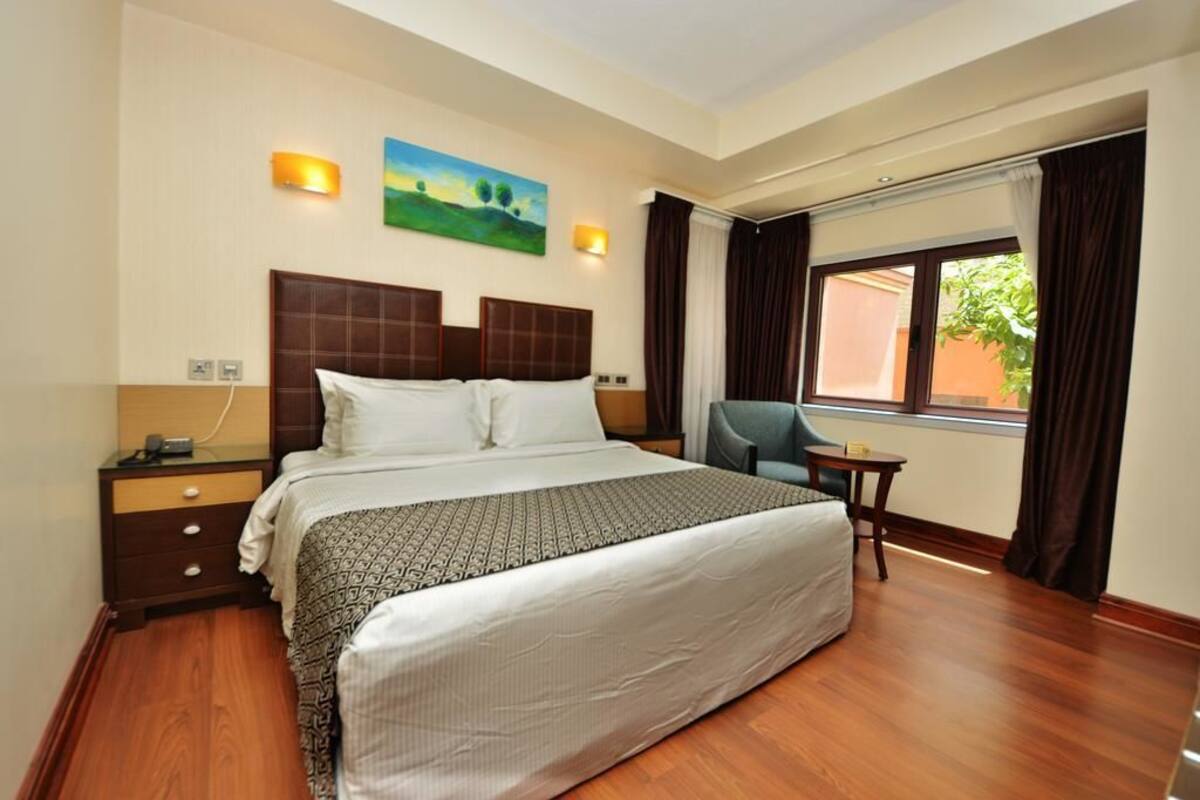 Une chambre d’hôtel avec un grand lit, une table de chevet, une chaise et une fenêtre avec des rideaux.