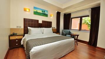 Quarto de hotel com uma cama grande, uma mesinha de cabeceira, uma cadeira e uma janela com cortinas.