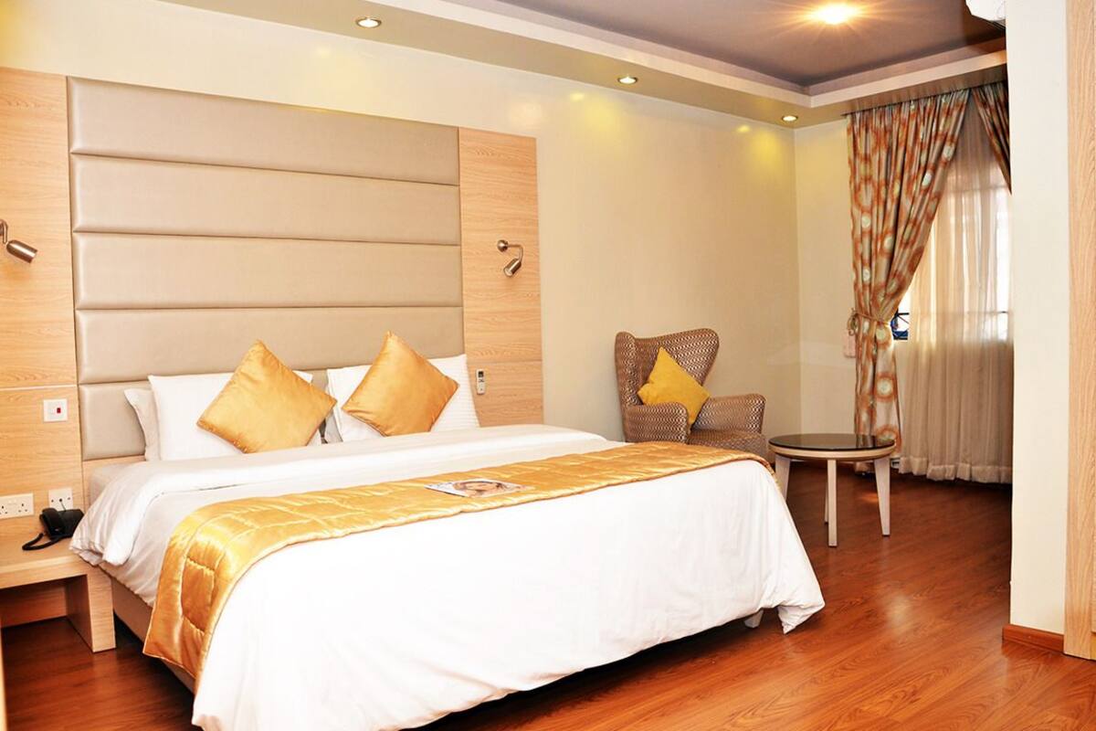 Une chambre d’hôtel avec un grand lit, une chaise, une petite table et une fenêtre avec des rideaux.