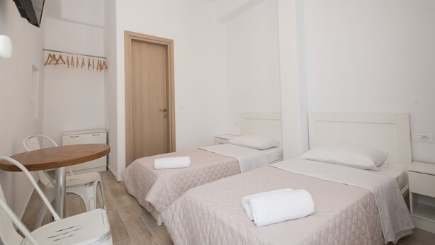 A hotel room with two beds, a small table, a chair, a desk, and a wardrobe. - Lovely Studio In Mykonos Old Town (Mykonos)
