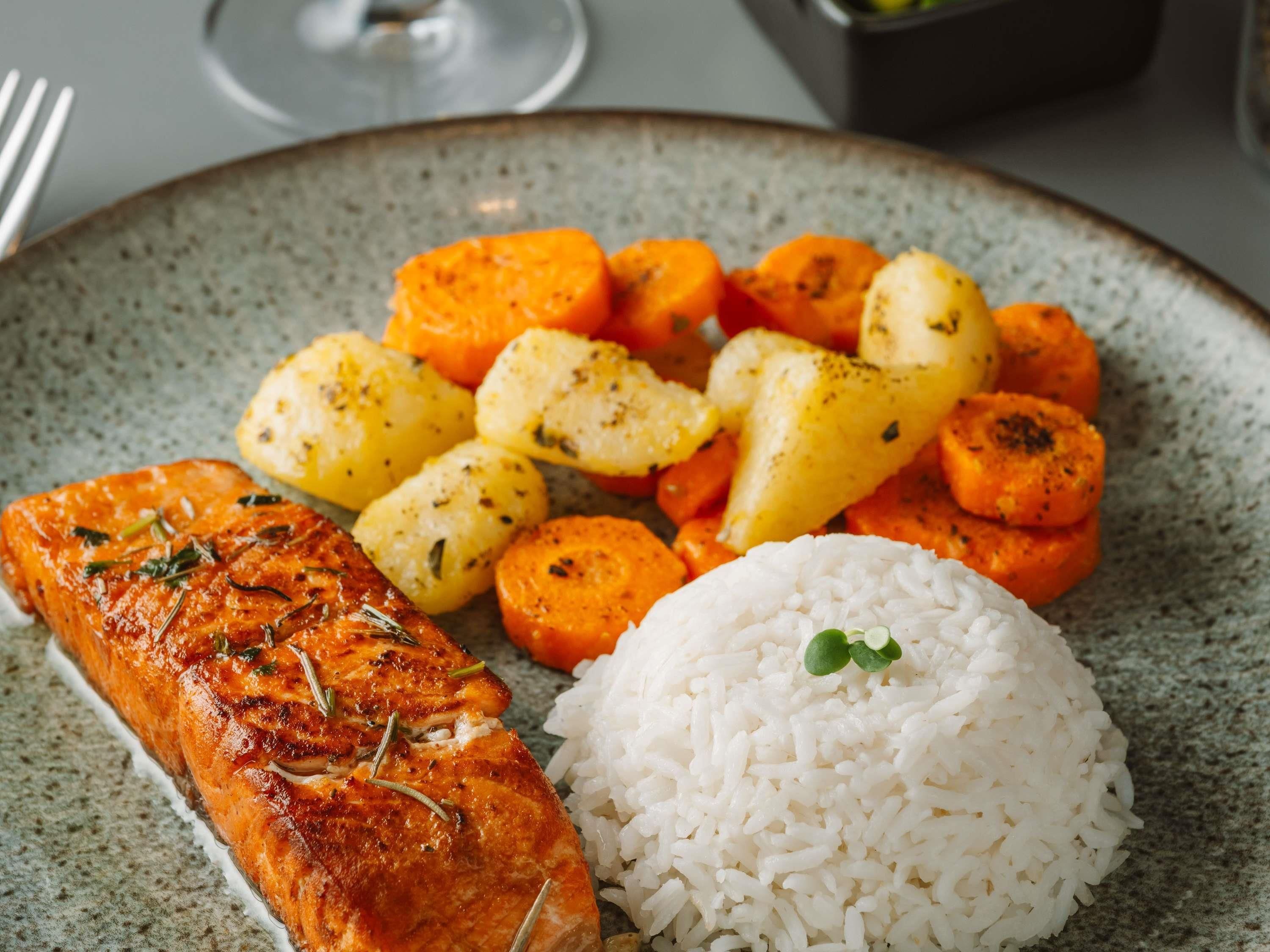 Un plato con salmón a la parrilla, papas asadas, zanahorias y arroz blanco.