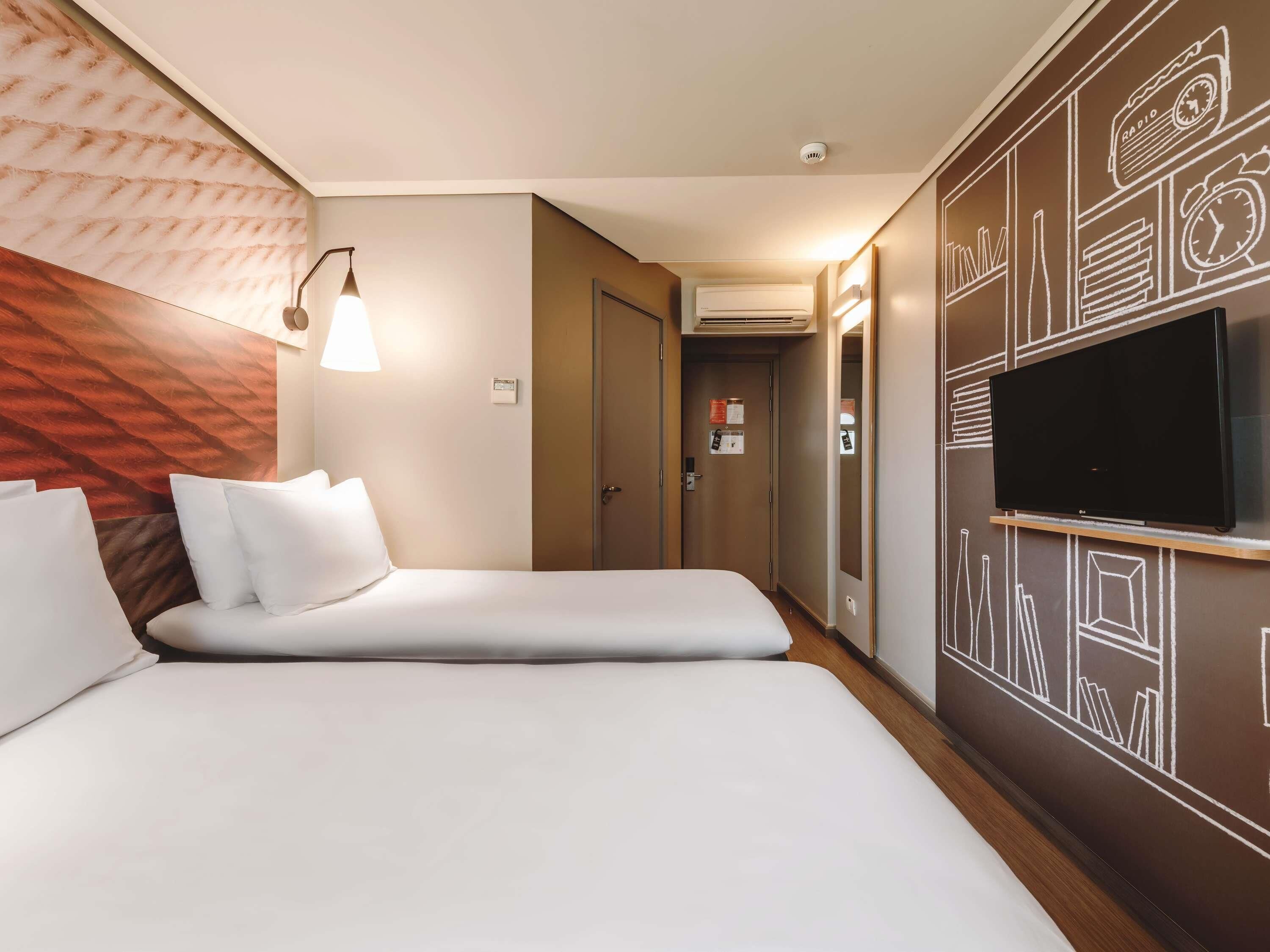 A hotel room with a bed, a TV, a lamp, and a wall with a geometric pattern.