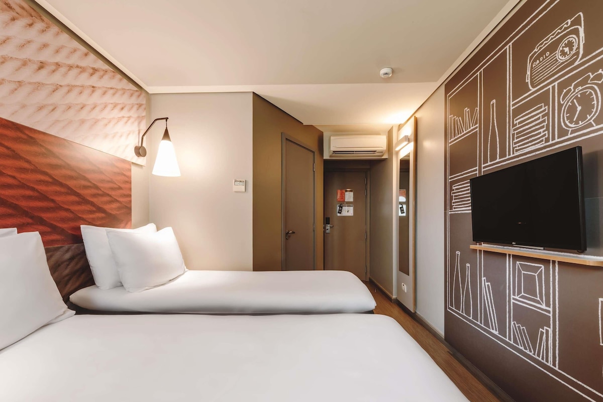 A hotel room with a bed, a TV, a lamp, and a wall with a geometric pattern.