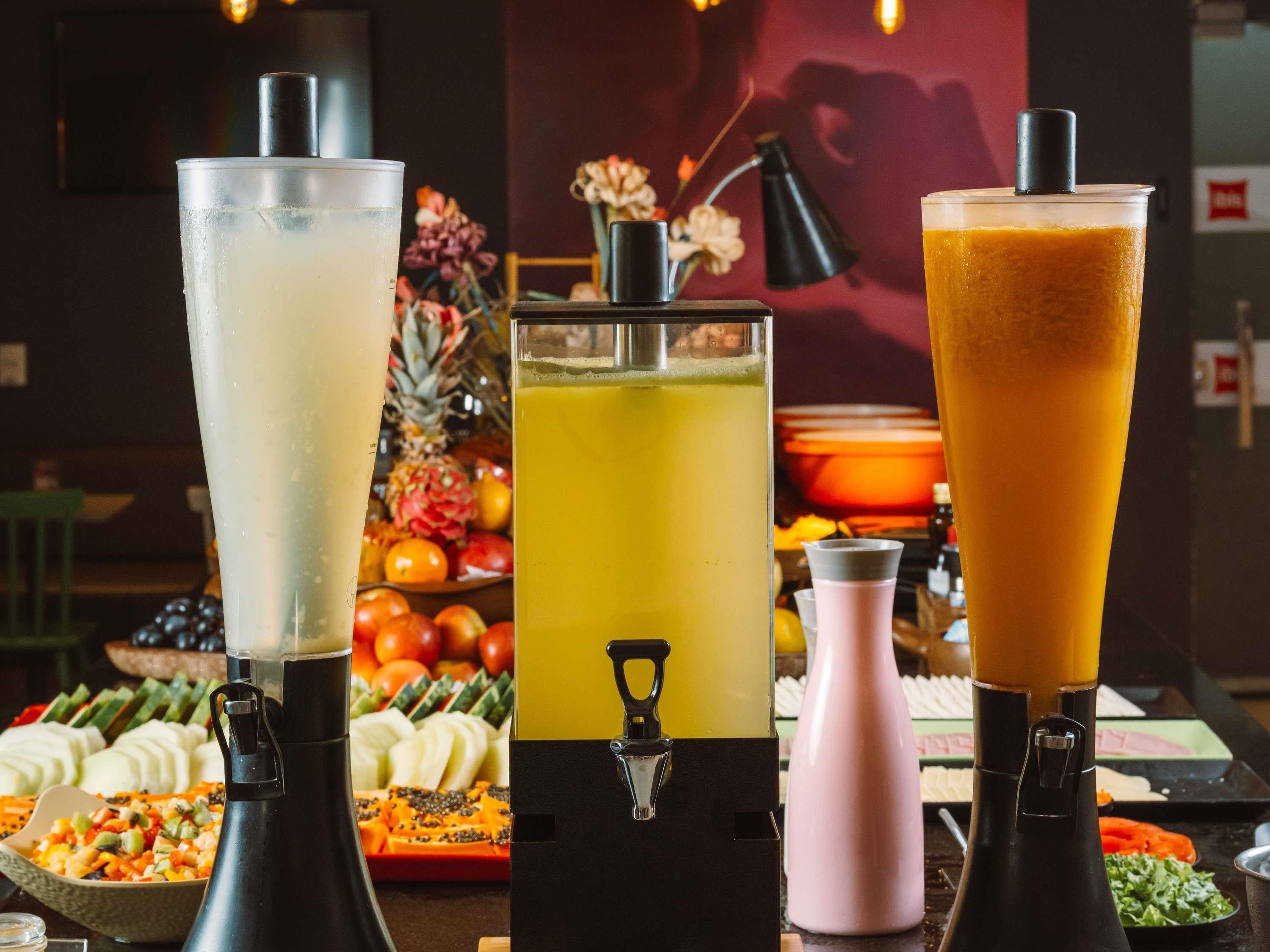 Three beverage dispensers with different colored drinks, a fruit platter, and a salad bar in the background.
