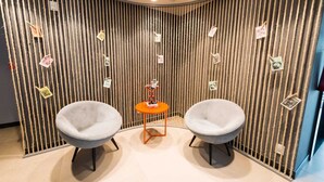 A room with two grey armchairs, a small orange table, and a vertical striped wall with pictures. - ibis Juazeiro do Norte (Juazeiro do Norte)