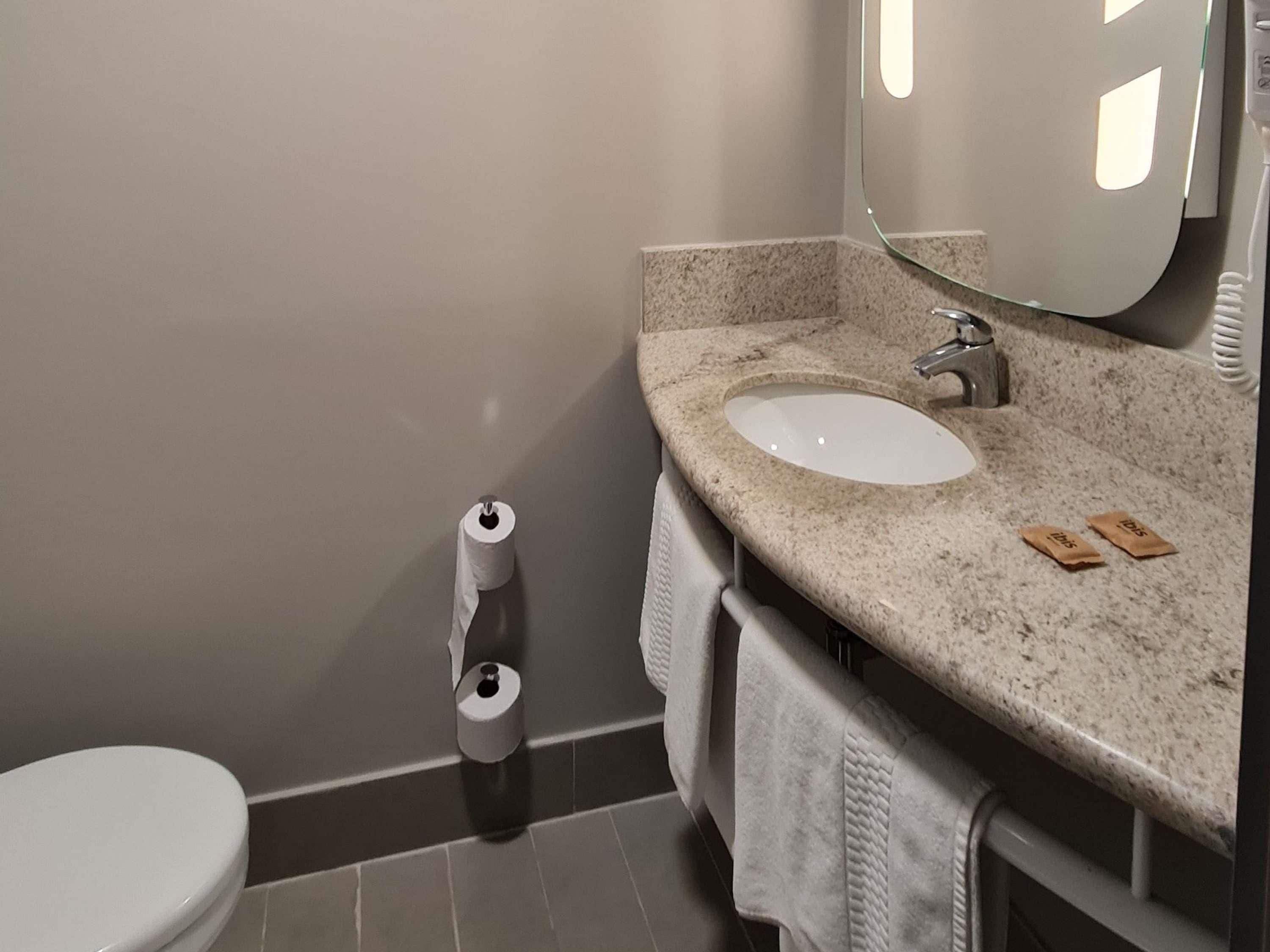 Ein Badezimmer mit Toilette, Waschbecken, Spiegel und einer Toilettenpapierrolle.