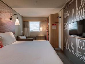 A hotel room with a bed, a TV, a desk, and a window with a view.
