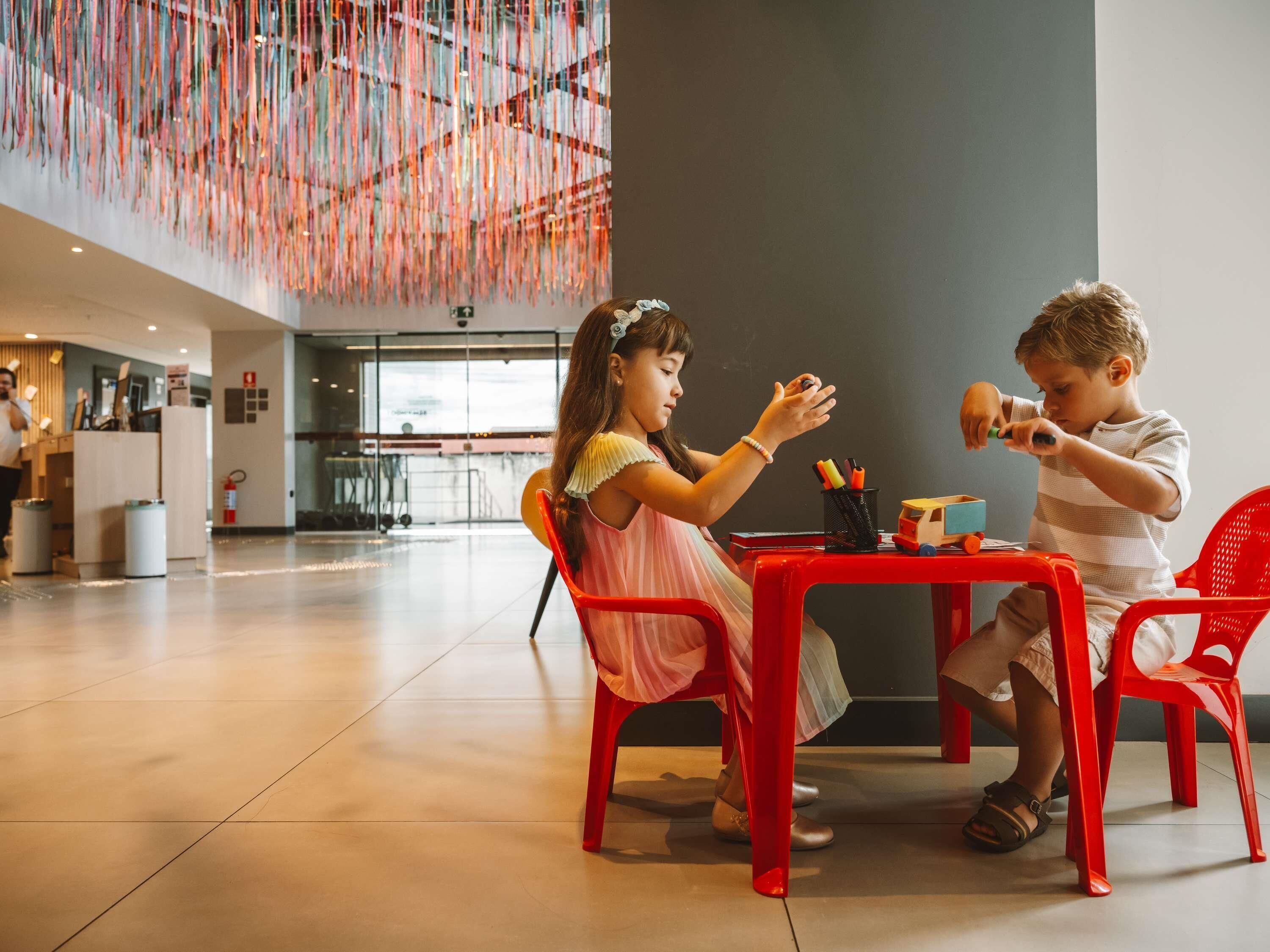 A spacious indoor area with a high ceiling and a modern design, featuring a dining table with chairs and a small table with toys.
