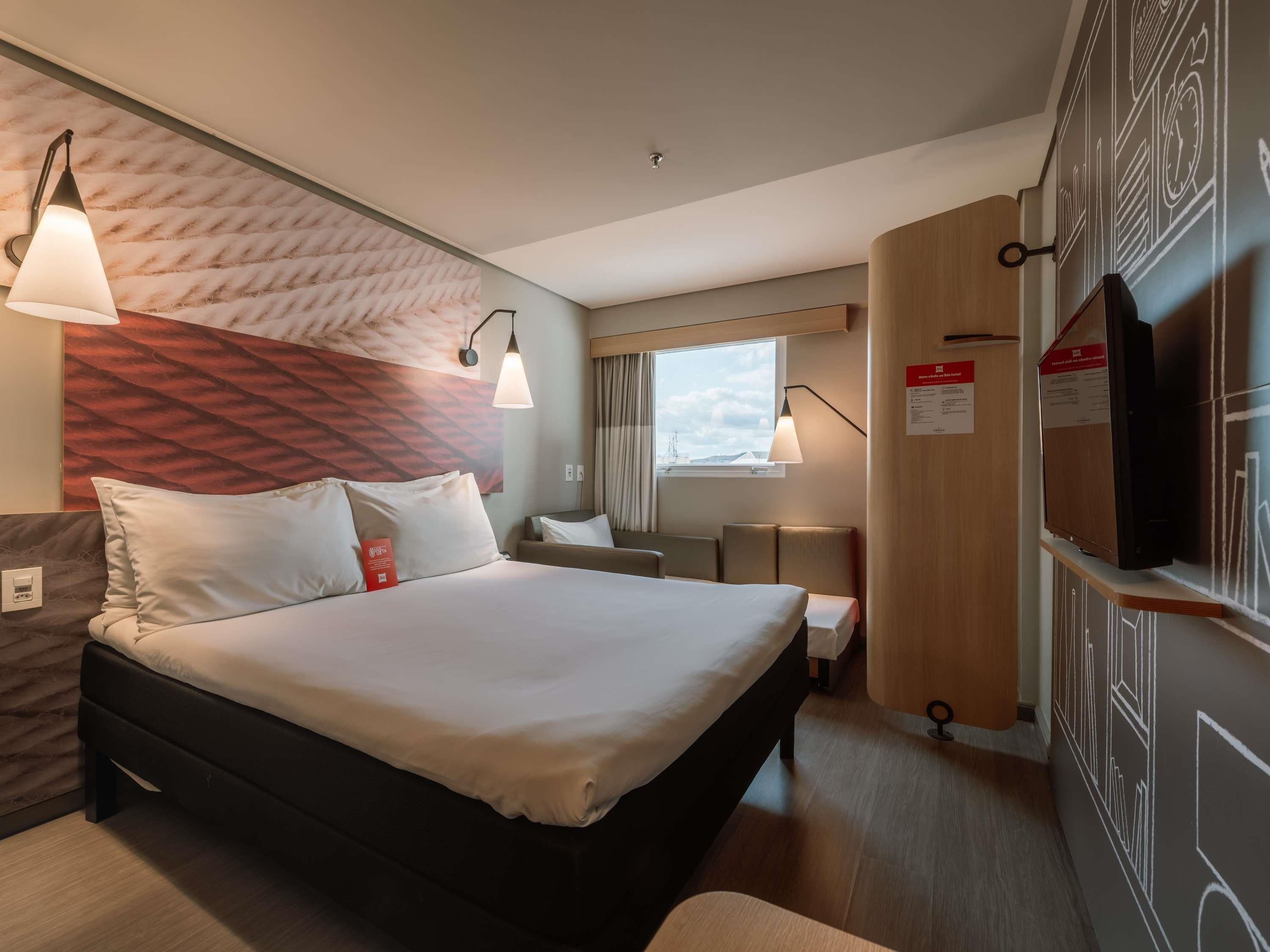 Et hotelværelse med en seng, sengeborde med lamper, et fjernsyn og et vindue med udsigt.