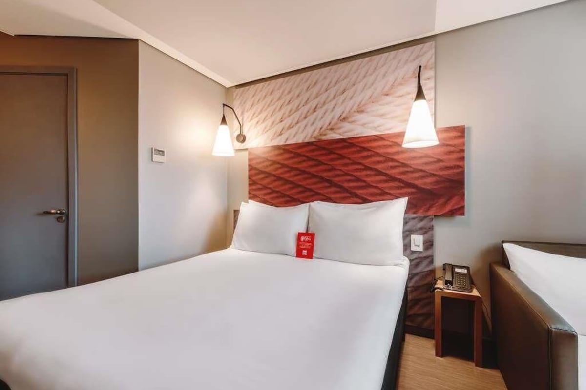 A hotel room with a large bed, a headboard with a textured design, bedside lamps, a telephone, and a small table.