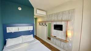 Et hotelværelse med en seng, et ophængt fjernsyn, en fastgjort aircondition og et spejl med hylde.