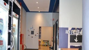 A corridor with a vending machine on the left, a table and chairs in the center, and a wall with a sign on the right. - ibis budget Itaperuna (Itaperuna)
