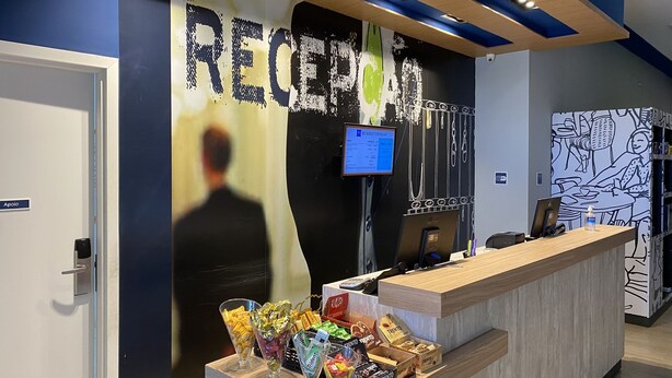 A reception area with a counter, a computer monitor, and a wall with a large 'RECEPTION' sign. - ibis budget Itaperuna (Itaperuna)