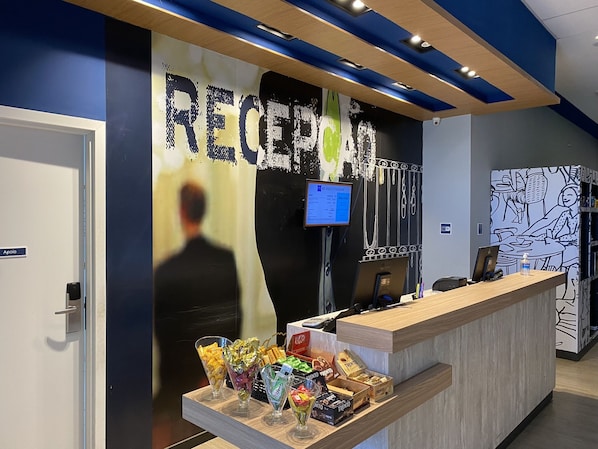 A reception area with a counter, a computer monitor, and a wall with a large 'RECEPTION' sign. - ibis budget Itaperuna (Itaperuna)