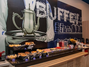 A buffet counter with various food items and a large coffee-themed mural in the background. - ibis budget Itaperuna (Itaperuna)