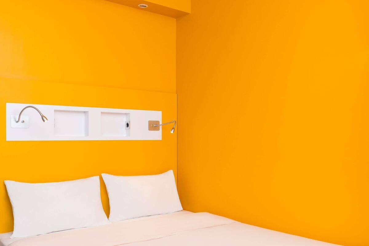 A bed with white bedding, a white headboard, and a white wall-mounted light fixture.