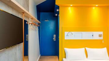 Quarto de hotel com uma cama, uma porta e um candeeiro fixado na parede.