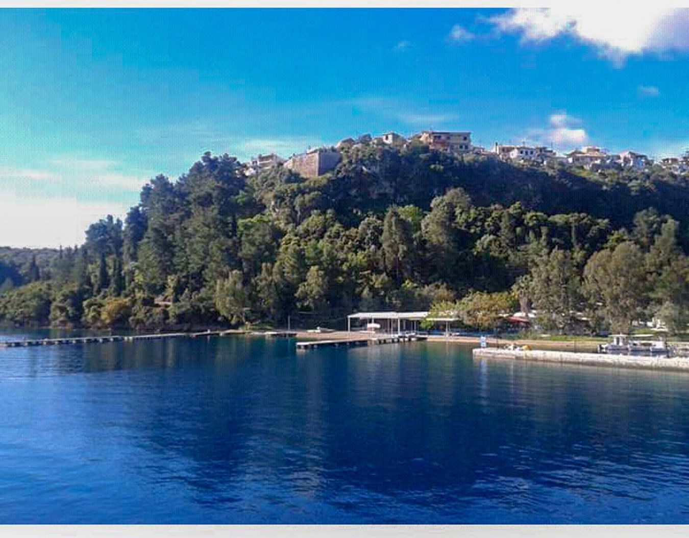 A coastal town with buildings on a hillside overlooking a calm body of water.