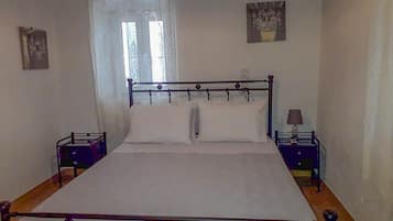 A bedroom with a metal-framed bed, two nightstands, a window with lace curtains, and a wall-mounted lamp.